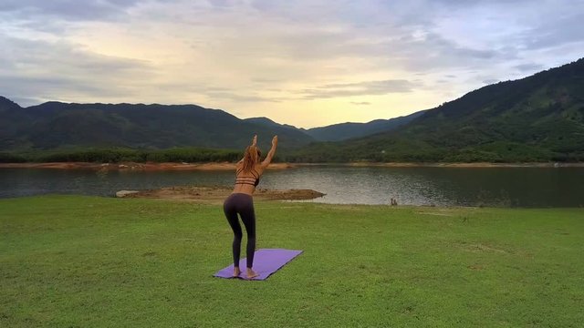 Drone Shows Girl Stands in Yoga Pose on Mat against Hills