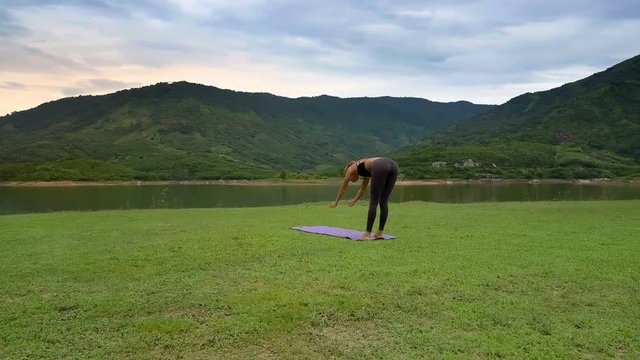 Flycam Side View Girl Holds Yoga Pose on Lake Bank by Hill