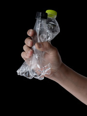 Hand holding empty used water bottle for recycling over dark background