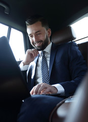 Caucasian male business executive travelling by a car and working on laptop computer.