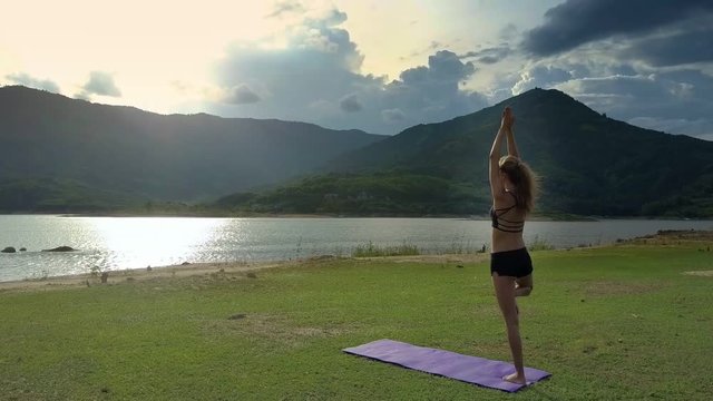 Flycam View Girl Stands in Yoga Pose against Shining River