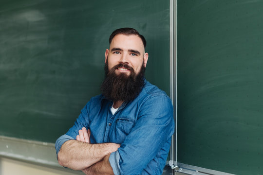 Smiling bearded man standing by blackboard