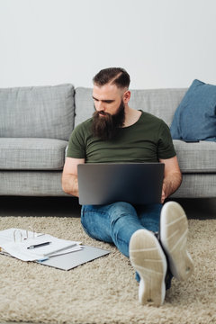 Man sitting of floor next to sofa with laptop