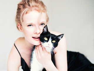 Pretty young woman with black cat in blanket in white bedroom