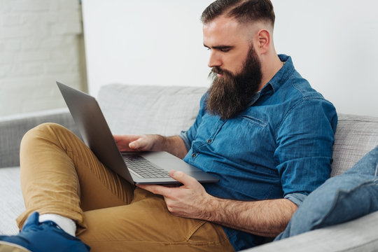 Bearded man sitting on sofa with laptop