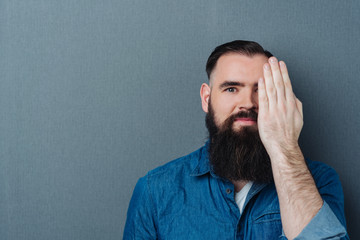 Bearded man covering one eye with his hand