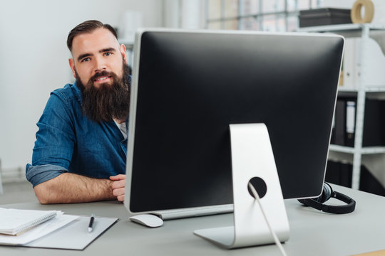 Smiling bearded man sitting in front of monitor
