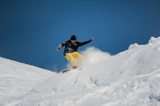 Freeride snowboarder at jump in high mountains at sunny day