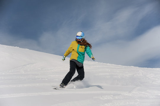 Female snowboarder in helmet and glasses riding down the mountain slope