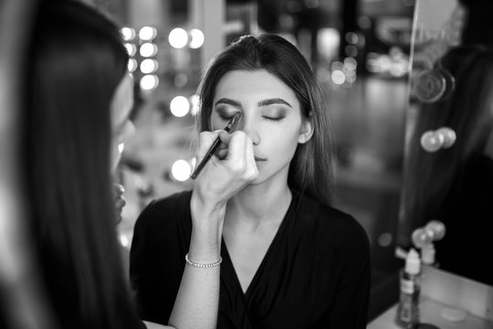 Professional makeup artist working with beautiful young woman. Fashionable Female Model With Soft Skin, Perfect Makeup And Fake Eyelashes. High Resolution
