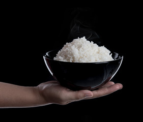 Hand holding a bowl with cooked rice on black background