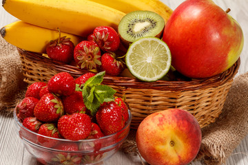 Fresh strawberries  in the glass bowl, nectarine, lime, kiwi, banana, apple in a wicker basket