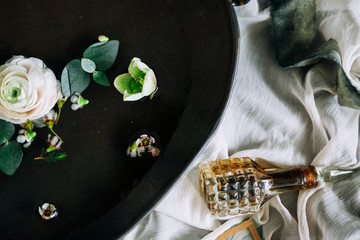 close-up of an antique black tray with water and flowers and a glass bottle with perfume on a blue and white cloth