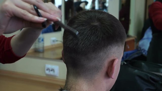 Barber cuts the hair of the client with scissors, close up.