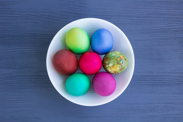 Fototapeta premium White plate with Easter versicolored eggs on grey wooden background
