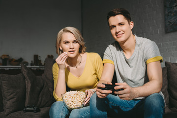 girlfriend eating popcorn and watching boyfriend playing video game at home