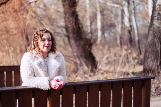 Outdoor close up portrait of beautiful curly woman wearing fur coat at park