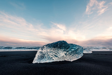 Ice on the black volcanic beach near Jokulsarlon glacier lagoon, winter Iceland. Detail of a glacial fragment of ice at black sand beach in beautiful evening light. © 1tomm