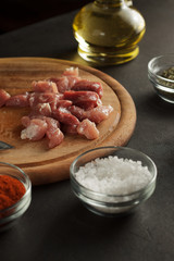 Pieces of raw meat on wooden cutting board with spices and bottle of oil.