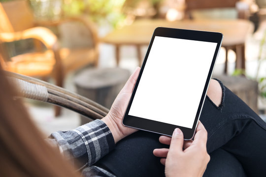 Mockup image of a woman holding black tablet pc with blank white screen sitting outdoor with  blur background in cafe