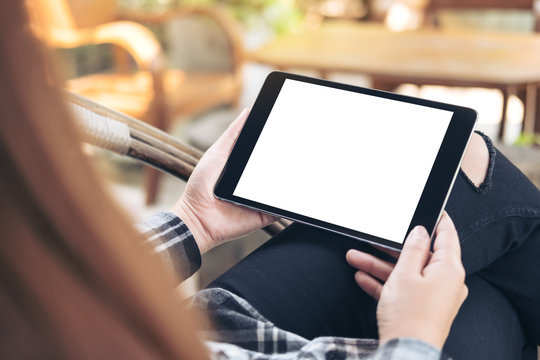 Mockup image of a woman holding black tablet pc with blank white screen sitting outdoor with  blur background in cafe