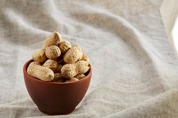 Unpeeled peanuts in ceramic bowl closeup, selective focus
