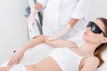 partial view of woman receiving laser hair removal procedure on arm made by cosmetologist in salon