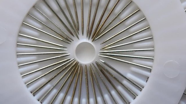 Abstract macro view. A seamstress woman pulls out and removes a sharp metal point ends pin needles with plastic head from a set of white discs. Dressmaker get a multi-colored needle and put it back