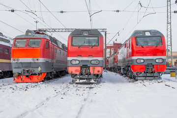 Three red electric locomotives are lined up on the railway in winter snow depot.