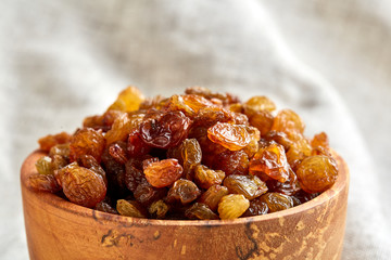 Wooden bowl with golden raisins on light tablecloth, close-up, selective focus