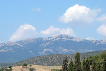 Panorama of the Crimean mountain range against the background of a cloudy blue sky.