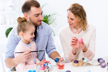 Parents helping daughter to color Easter eggs