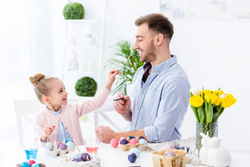 Young man and child girl painting Easter eggs
