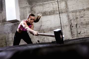 Fitness woman hitting wheel tire with hammer sledge in the gym, cross fit training.