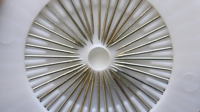 Abstract macro view. A seamstress woman pulls out and removes a sharp metal point ends pin needles with plastic head from a set of white discs. Dressmaker get a multi-colored needle and put it back