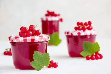 Homemade red currant jelly in the glass jars, green leaves and fresh berries on a white wooden table.