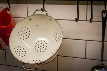A white metal colander, a kullerder or strainer is hanging on the kitchen wall.
