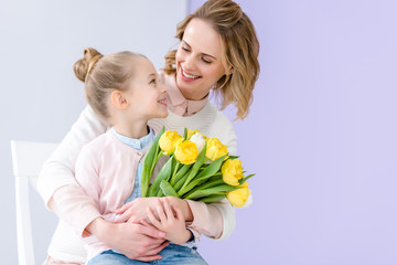 Cute child embracing mother with tulips bouquet on 8 march