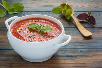 Gazpacho soup with fresh basil in a white bowl on the wooden rustic table.