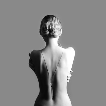 Art Nude fashion Nude back of blonde woman on grey background. Girl hugs herself with her hands