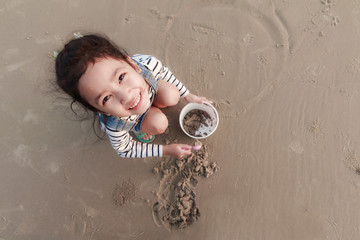 Naklejka premium Top view portriat Asian little girl playing on the sand beach with evening ambient