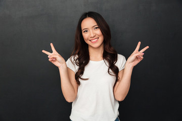 Pleased asian woman in t-shirt showing peace gestures