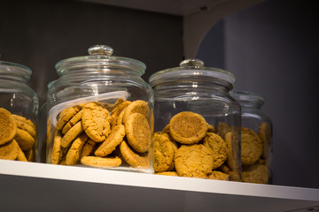 Chocolate biscuits in a glass jar on a wooden shelf.