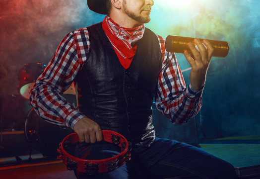 The actor plays on a tambourine and a shaker.