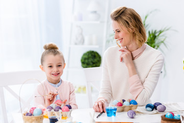 Young woman and child girl painting Easter eggs