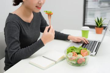 Young woman eating salad while working at desk. Weight loss concept