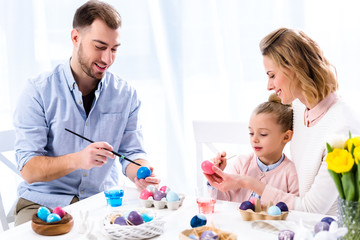 Obraz na płótnie Canvas Family coloring Easter eggs with painting brushes