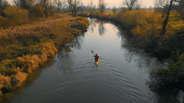Medium aerial tracking shot of yellow kayak paddling on calm river in beautiful nature.
