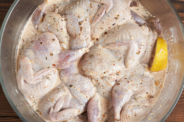 Quails marinated in spices with lemon in a glass saucepan. Close-up.