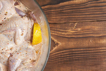 Quails marinated in spices with lemon in a glass saucepan on a wooden background. Close-up.